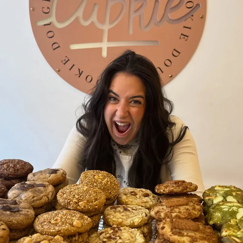 Megan Villiot, fondatrice de Cupkie, derrière une pile de cookies, sous le logo de la boutique