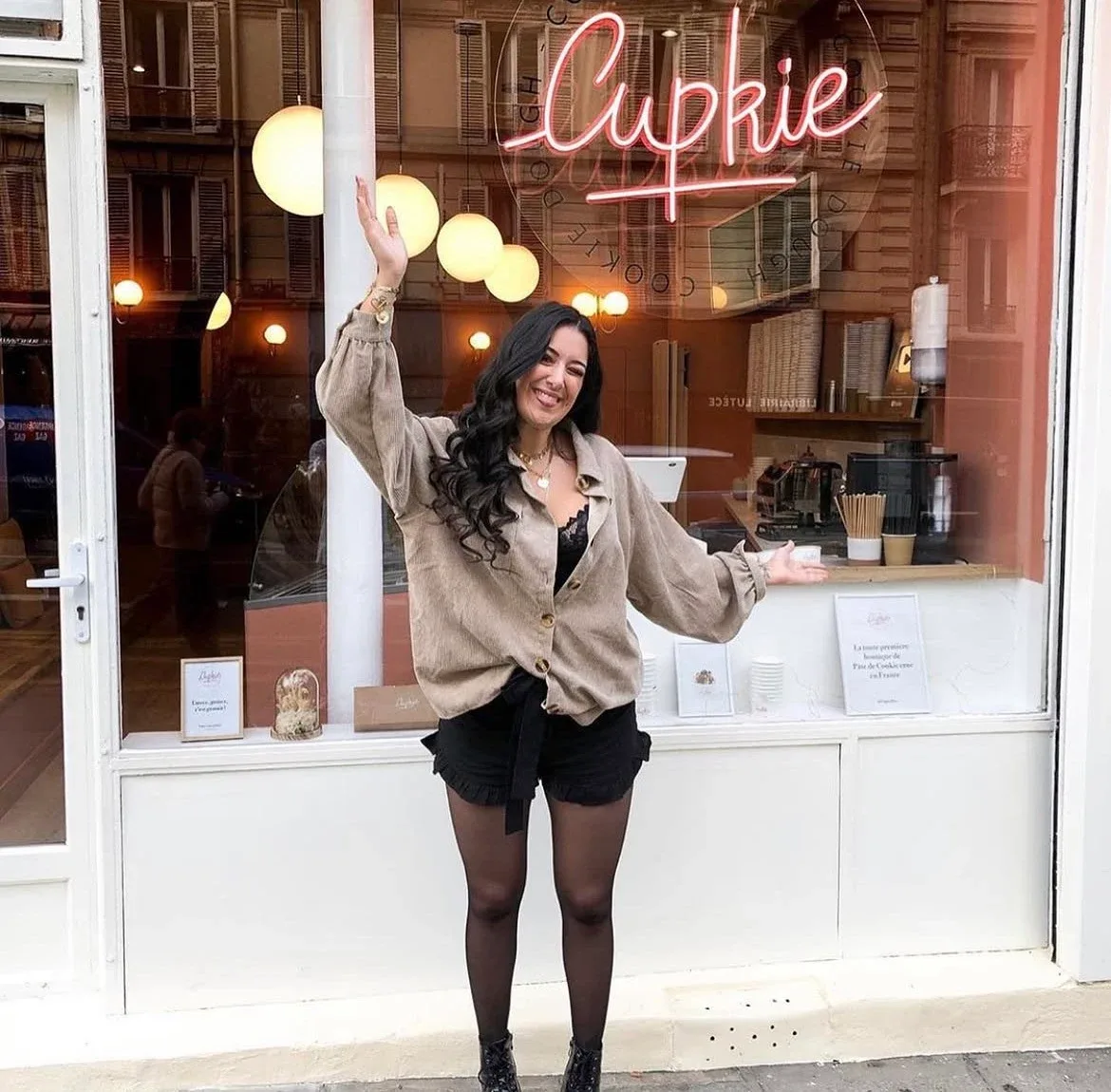Megan Villiot, bras levé, devant la vitrine de la boutique Cupkie et son néon rose