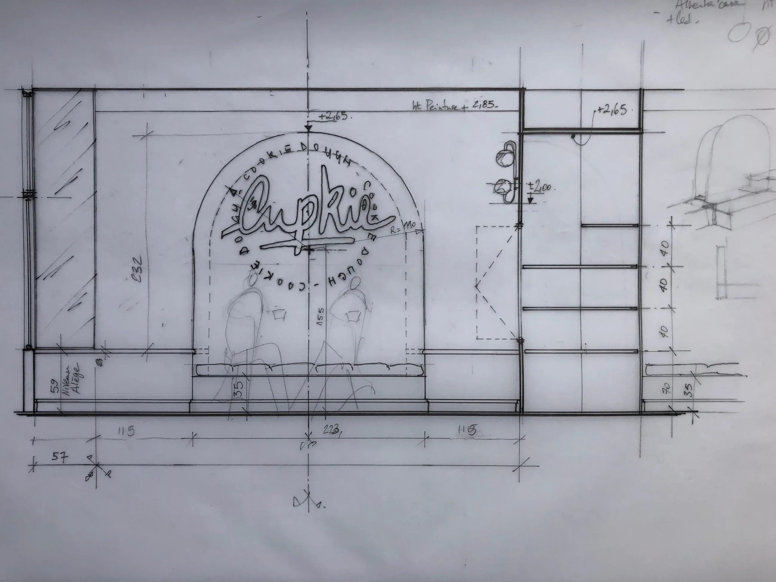 Plan d’élévation dessiné à la main : une alcôve en arc avec le logo Cupkie, une banquette et des étagères, avec les cotes du décorateur